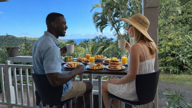 A couple dining at an outdoor table with a view of the ocean and lush greenery. - Studio, bas de Villa « La Marguerite » (Deshaies)