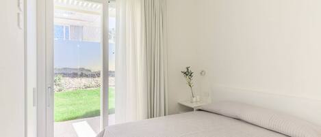 A bedroom with a bed, a nightstand, a potted plant, and a sliding glass door leading to a balcony.
