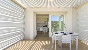Uma sala de jantar moderna com uma mesa posta para quatro pessoas, uma cozinha visível através de uma porta aberta e vista para o verde lá fora.