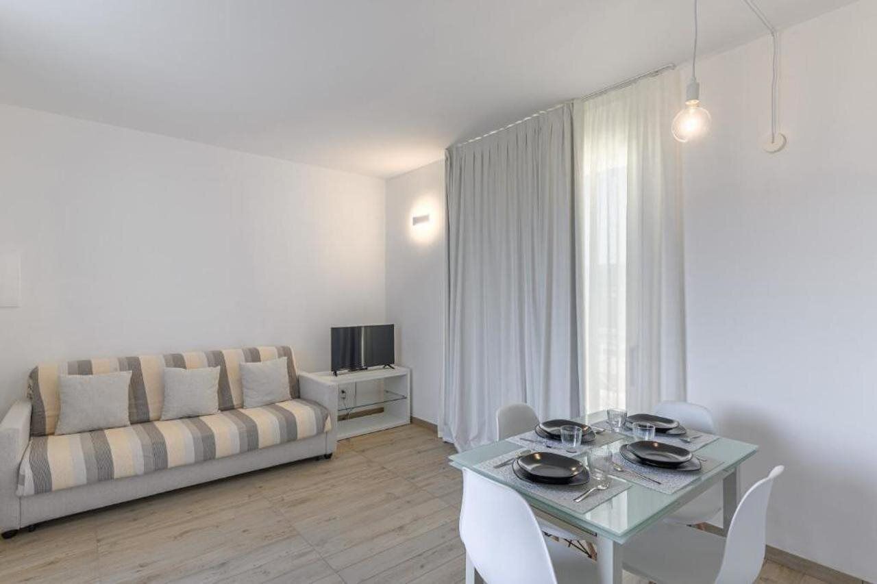 A modern living room with a sofa, a dining table set for two, and a TV on a side table.