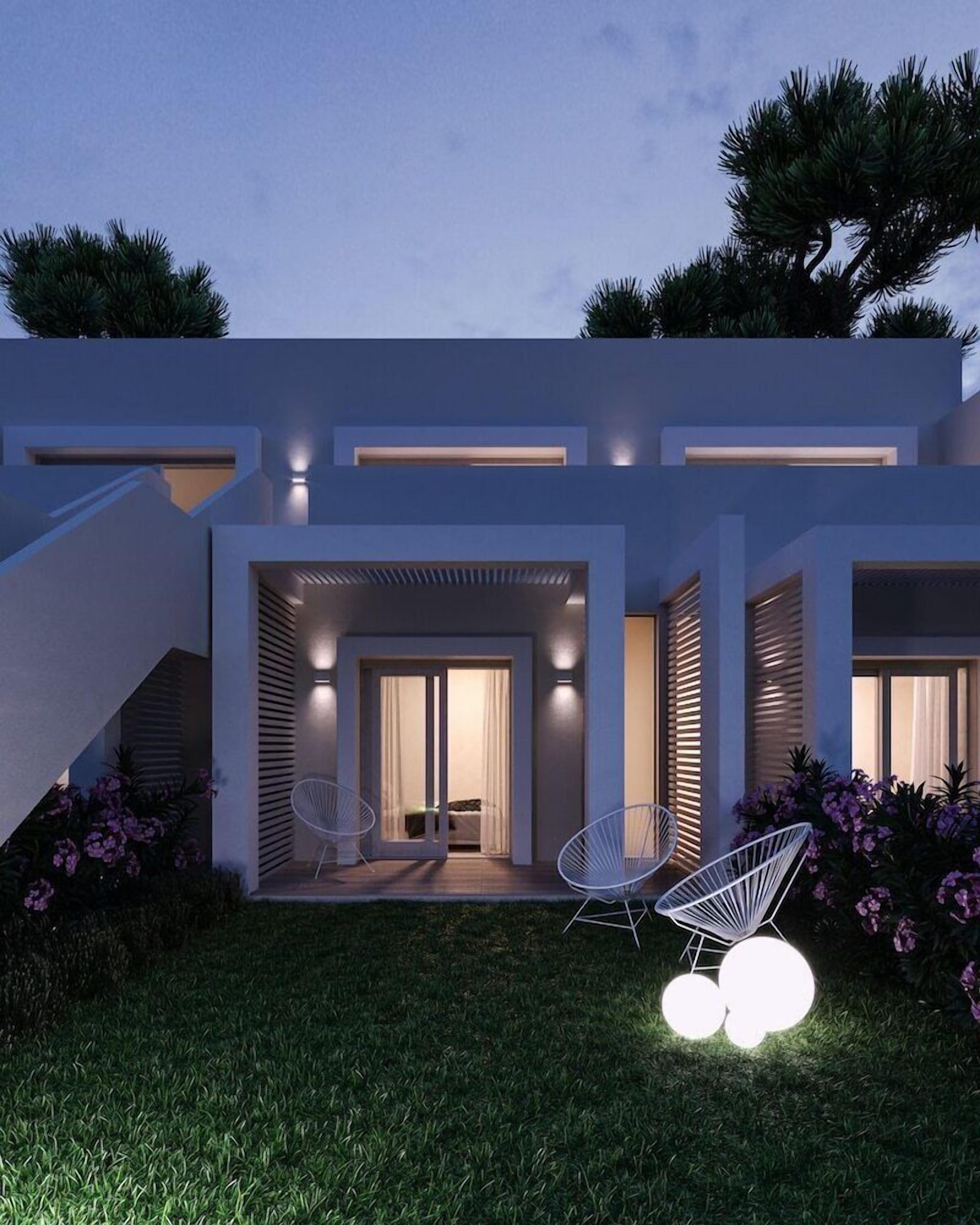 Ein modernes Haus mit einer überdachten Terrasse, zwei weißen Stühlen und einem kleinen Garten.