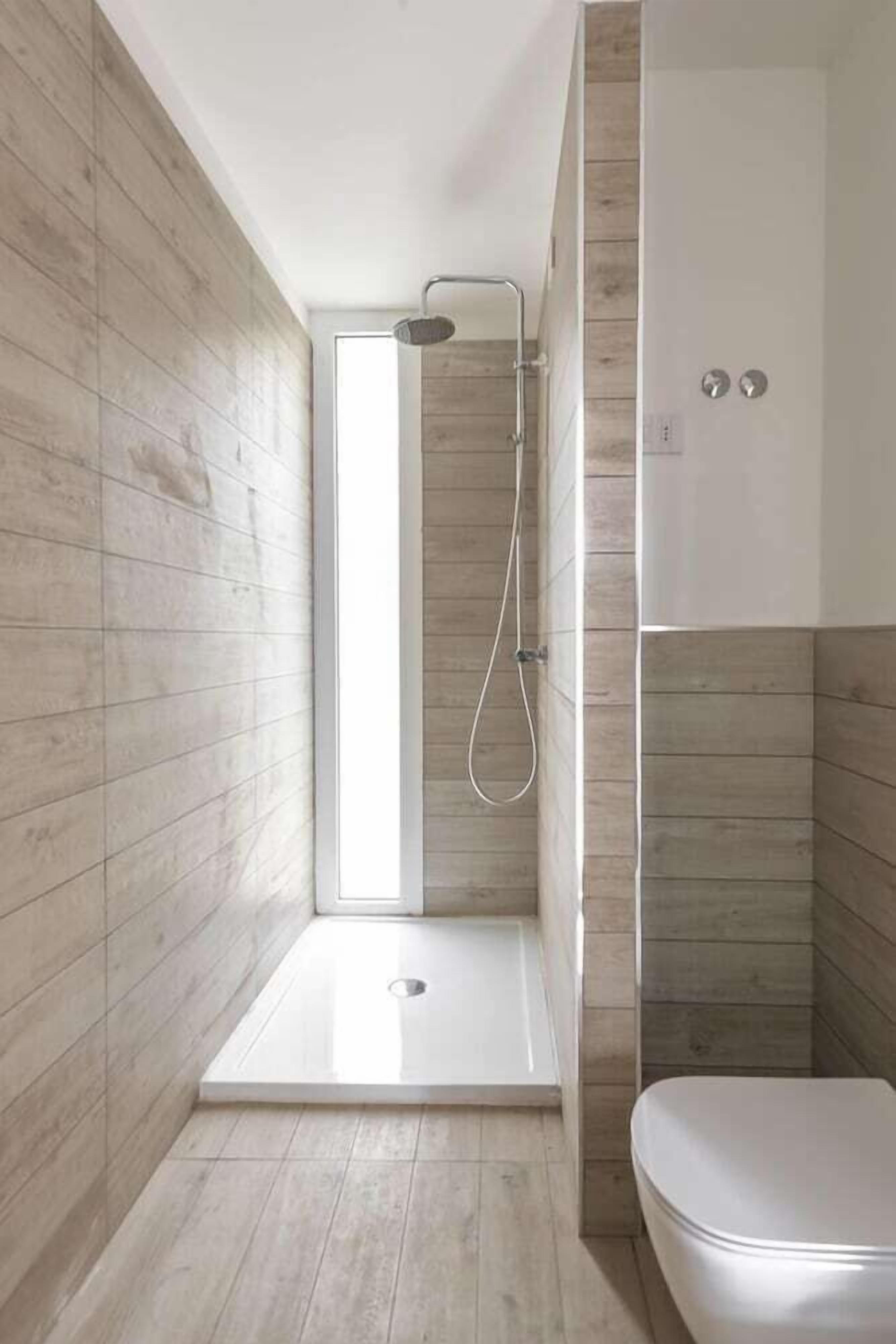 A modern bathroom with a shower, toilet, and a view of the outdoors.