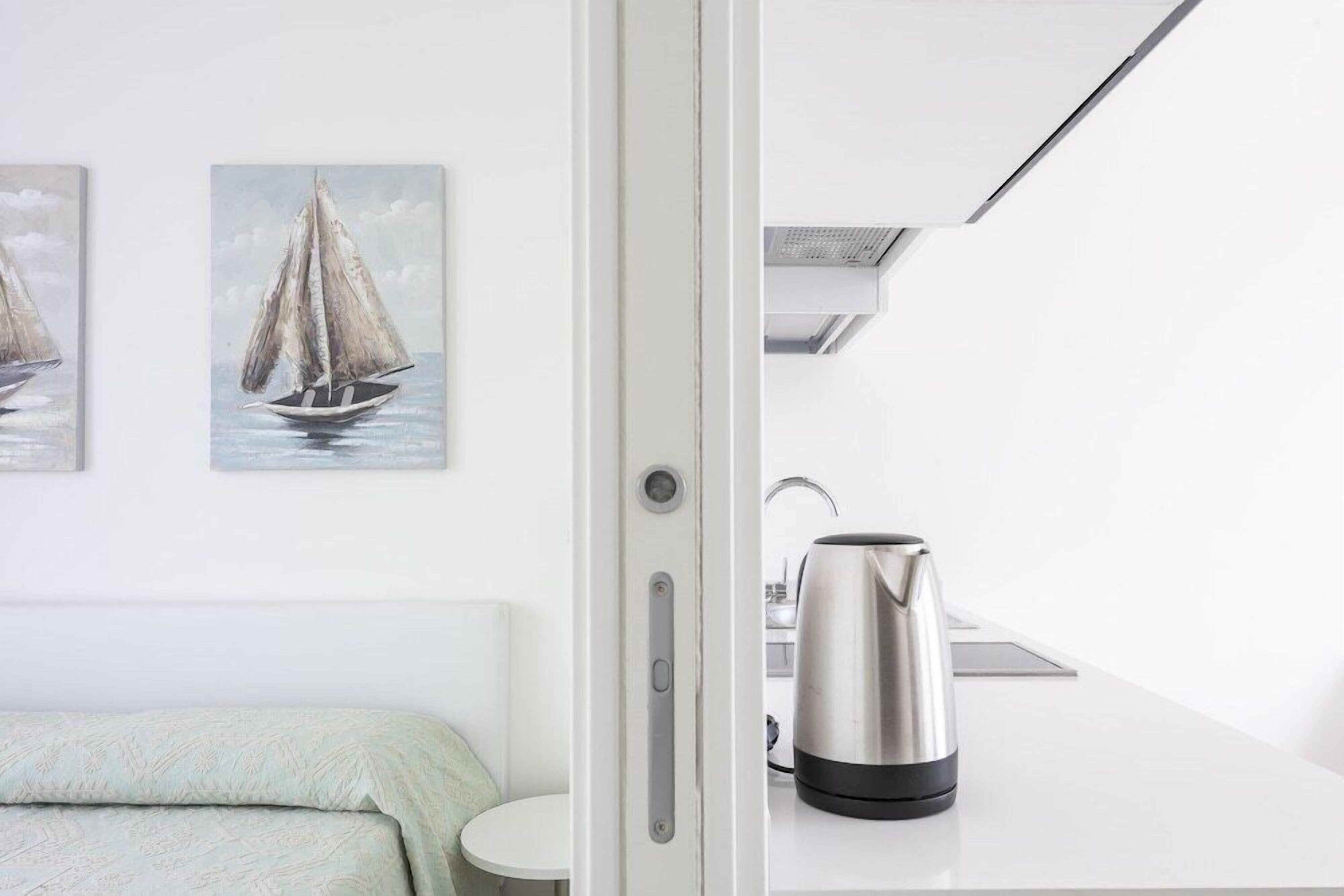 Una habitación de hotel moderna con una cama, una pequeña mesa redonda, una tetera y dos cuadros de veleros.