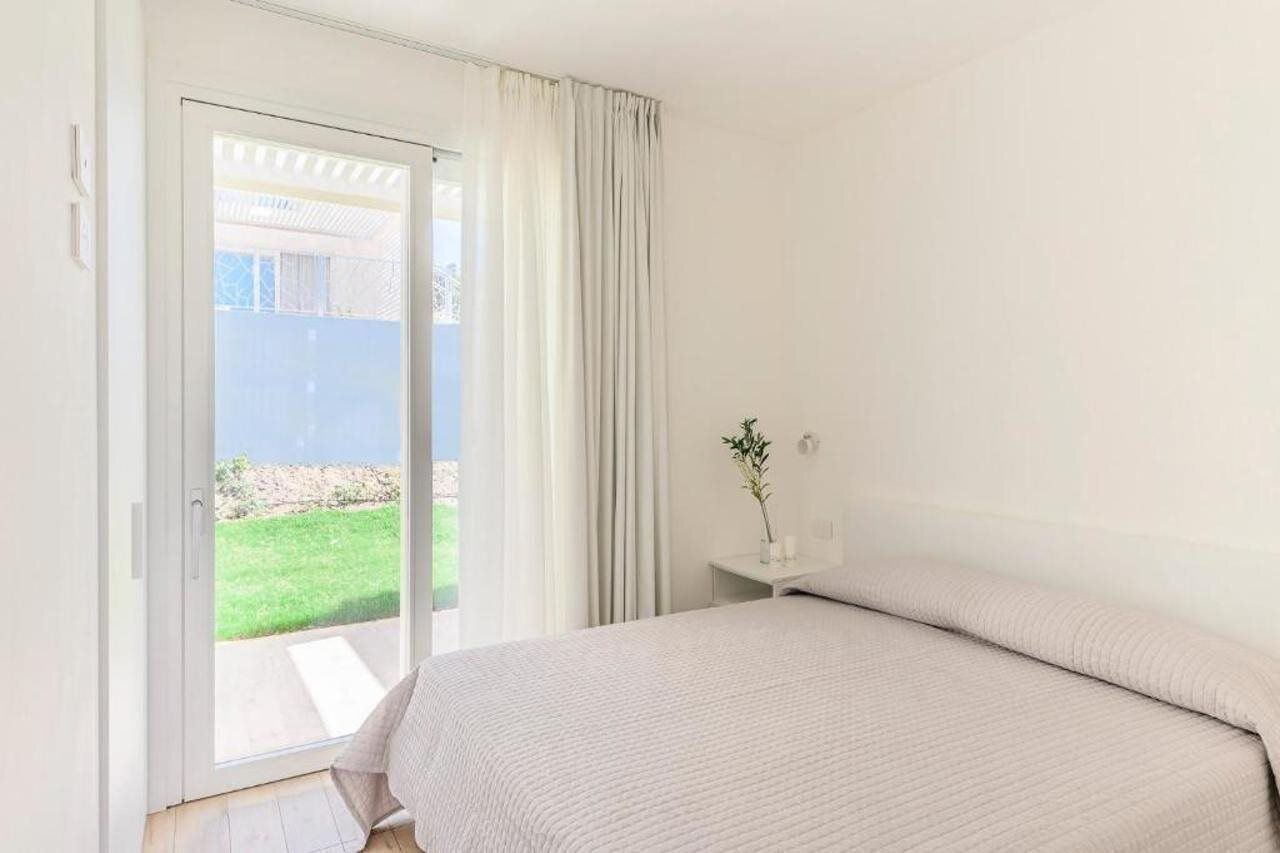 A bedroom with a bed, a nightstand, a vase with a plant, and a sliding glass door leading to a balcony.
