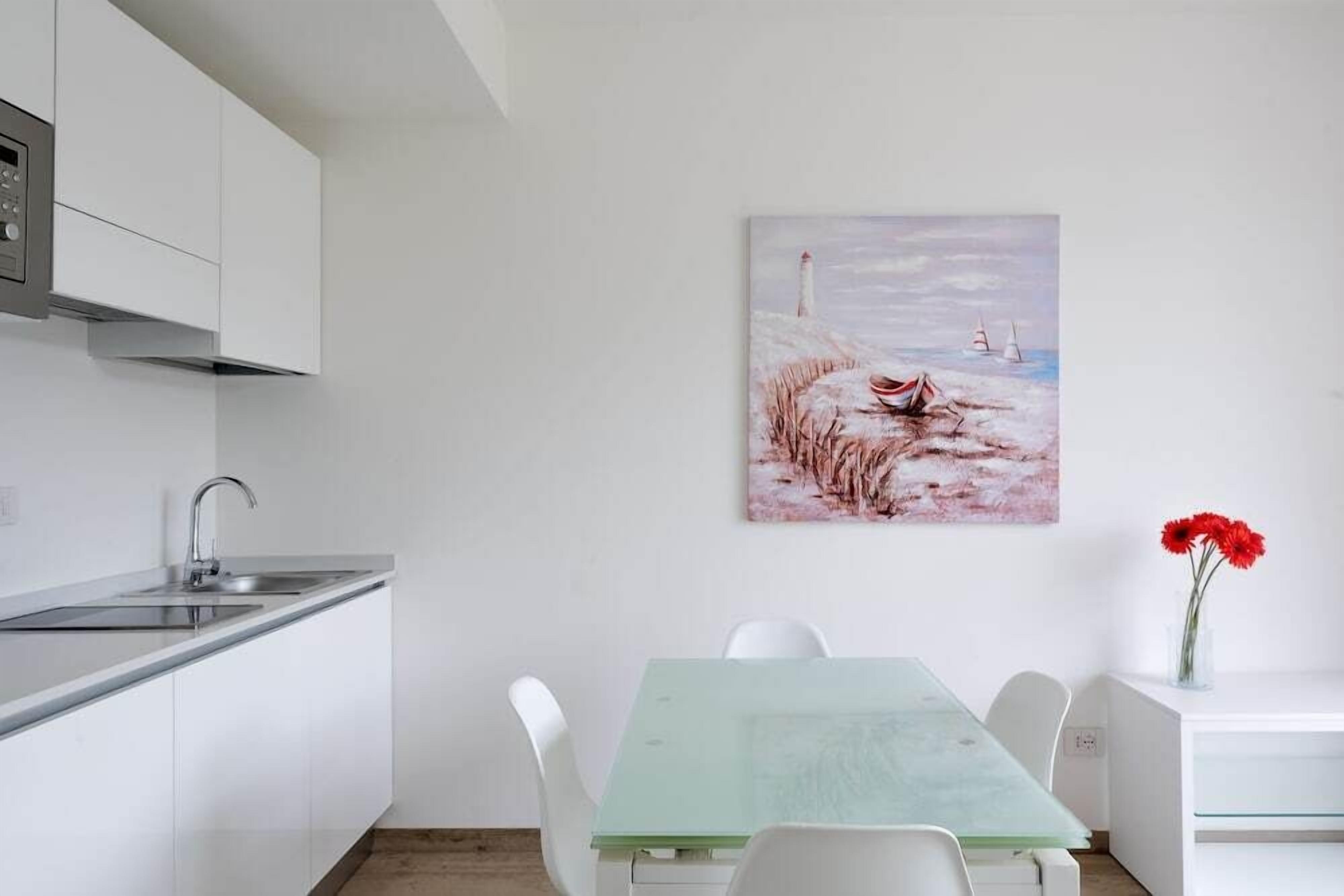 A modern kitchen with white cabinetry, a stainless steel sink, and a dining area with a glass table and white chairs.