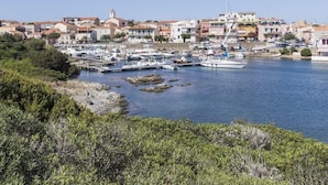 Uma marina costeira com barcos atracados, rodeada por edifícios residenciais com telhados de terracota.