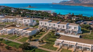 Uma área residencial costeira com casas brancas modernas, uma praia e águas azuis cristalinas.