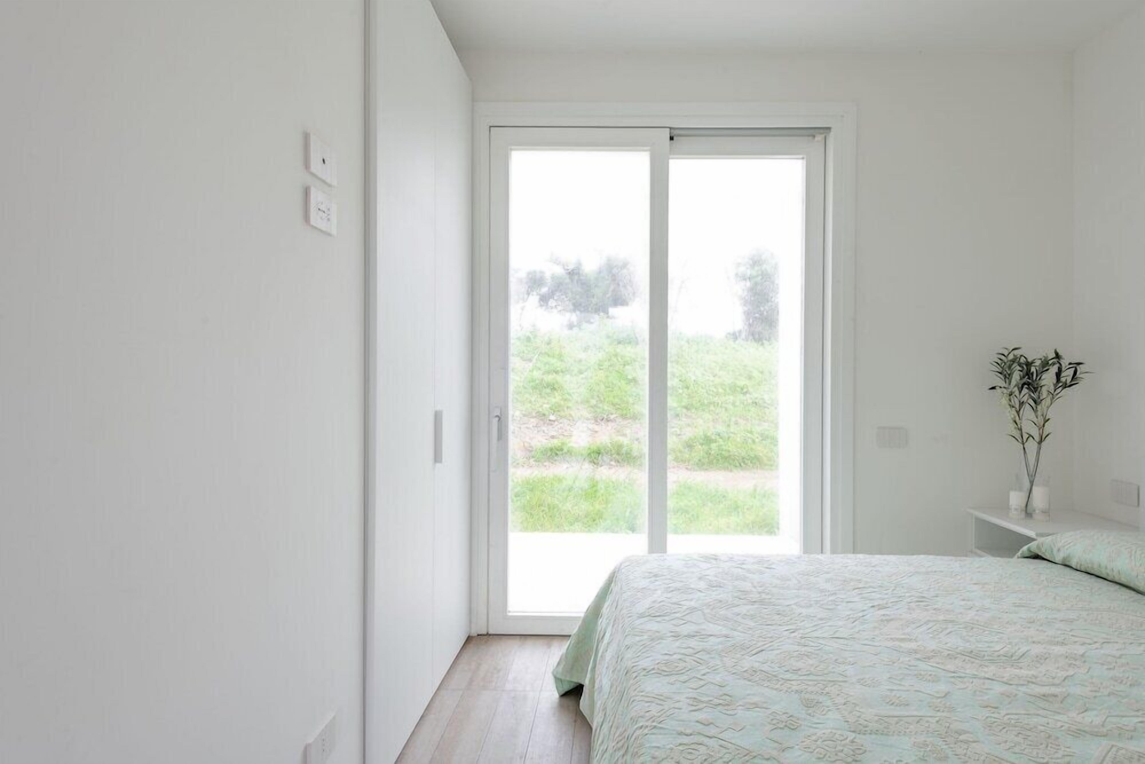 A bedroom with a large sliding glass door leading to a grassy outdoor area.