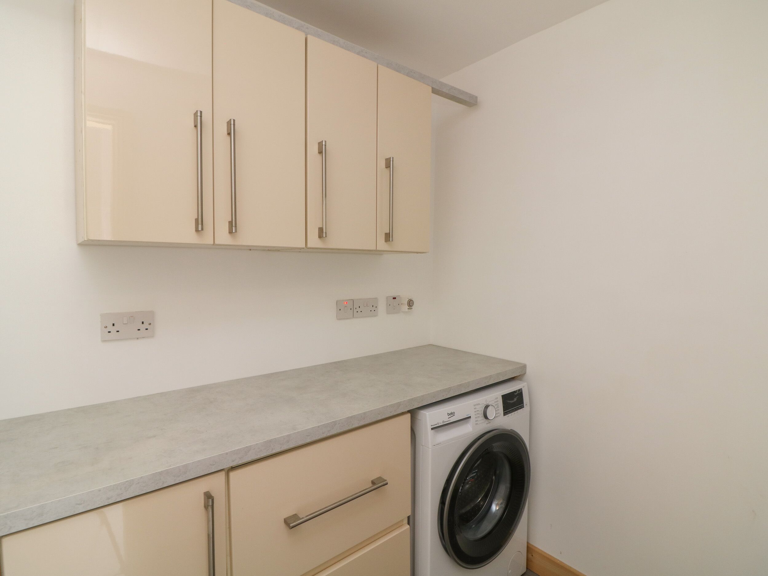 A compact laundry room with a washing machine, beige cabinets, and a countertop.