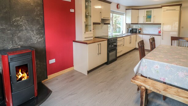 A modern kitchen with a wood-burning stove, white cabinets, and a dining area with a floral tablecloth.