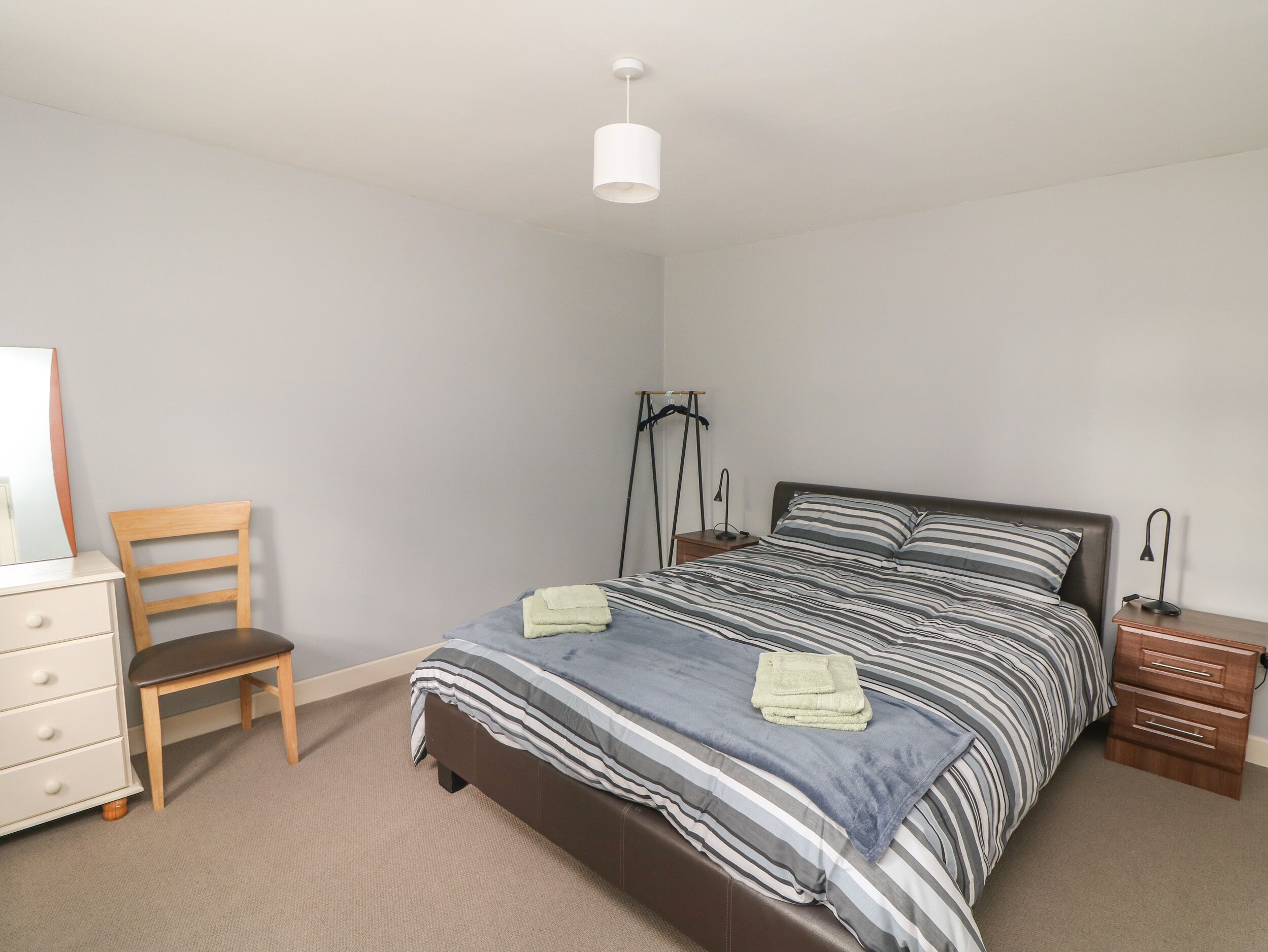 A bedroom with a bed, a chair, a dresser, and a hanging light fixture.