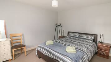 A bedroom with a bed, a chair, a dresser, and a hanging light fixture.