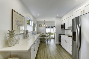 Una cocina moderna con armarios blancos, un refrigerador de acero inoxidable y un comedor con candelabro.