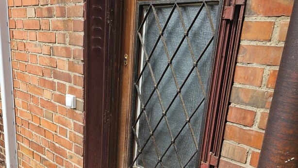 Uma porta de madeira com janela de grade de metal, um toque de latão e uma parede de tijolos.