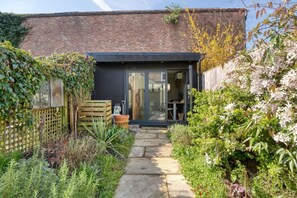A modern house with a glass door entrance, a stone pathway, and a garden with various plants and flowers. - Stylish 2BD with Private Garden and Sauna (Oxford)