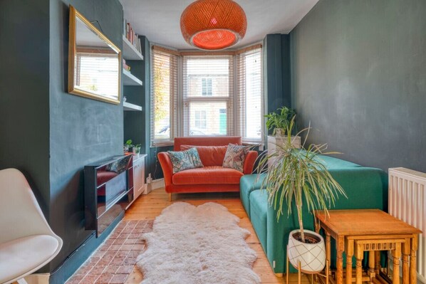 A cozy living room with a red sofa, a green armchair, a white chair, a large potted plant, and a wooden table. - Stylish 2BD with Private Garden and Sauna (Oxford)