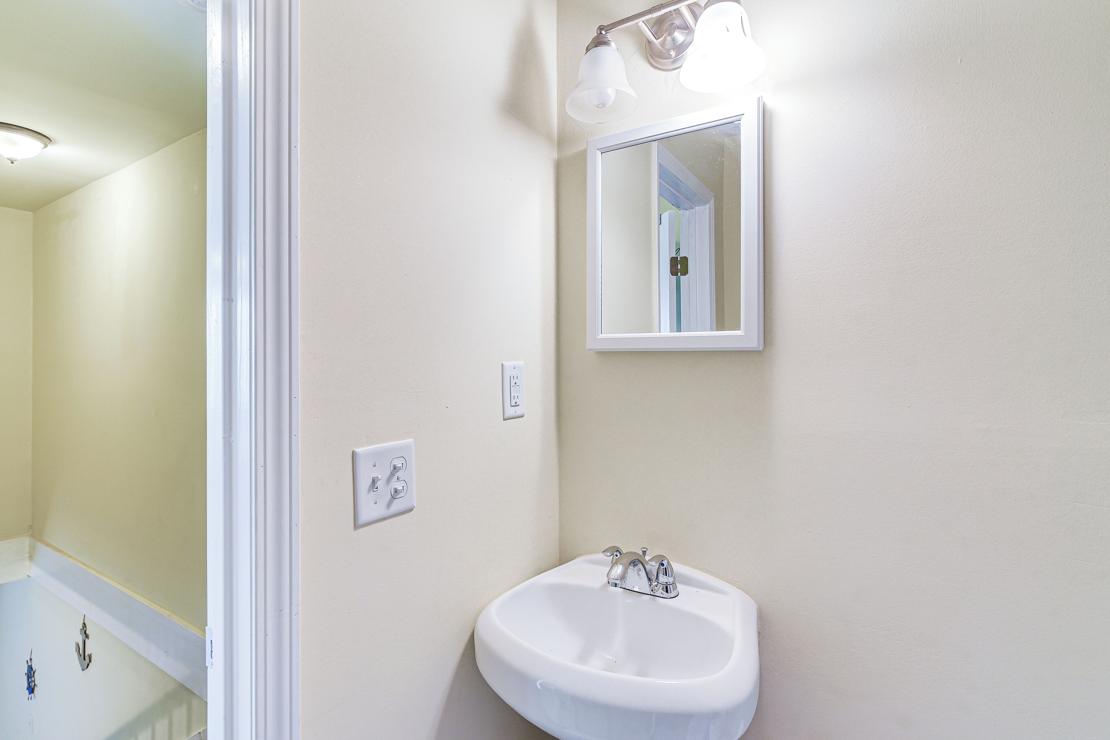 A bathroom with a white sink, a mirror, and a light fixture above the mirror.
