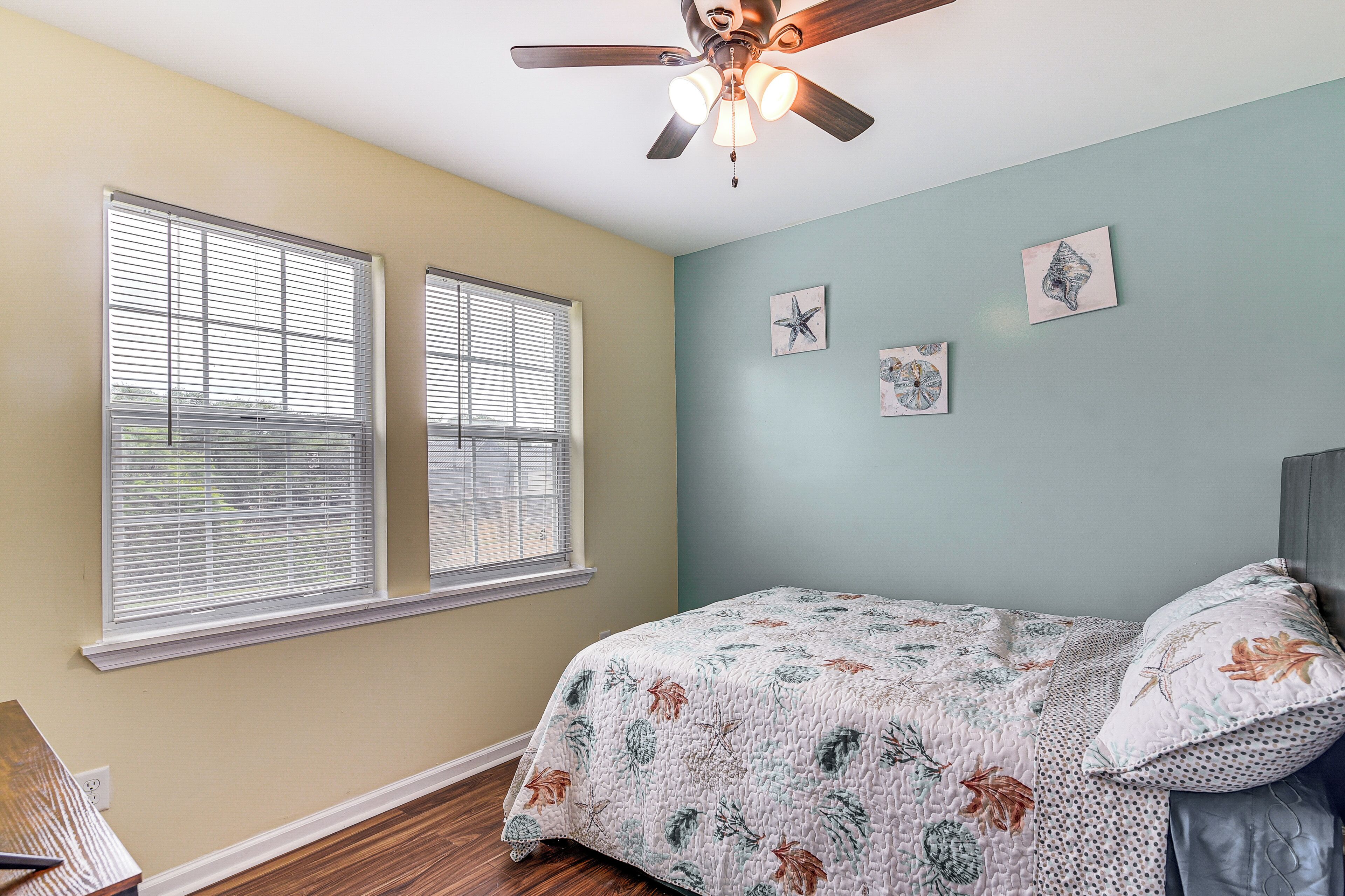 A bedroom with a bed, a ceiling fan, and two windows with blinds.
