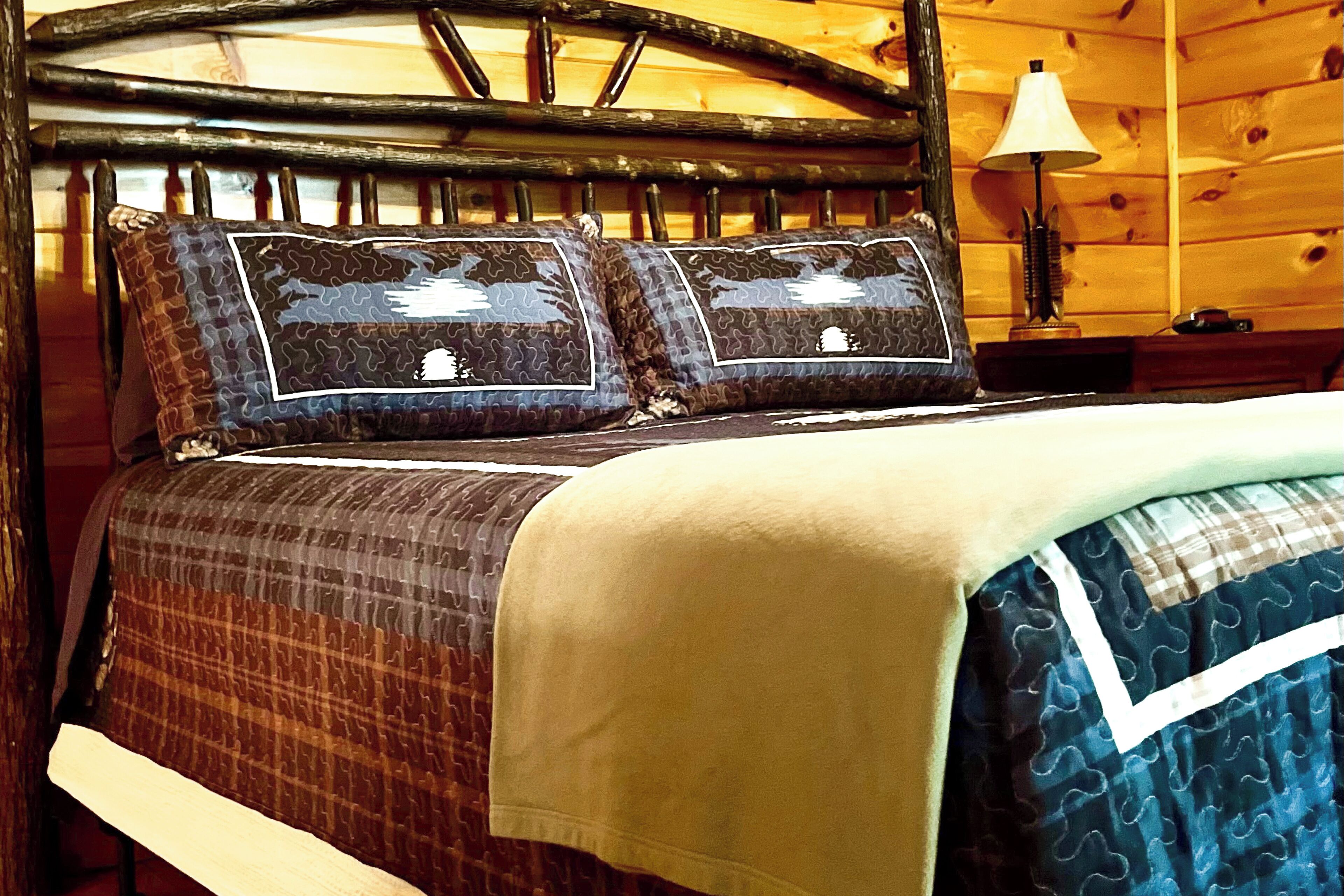 Habitación tipo cabaña de madera con una cama, almohadas estampadas y una colcha.