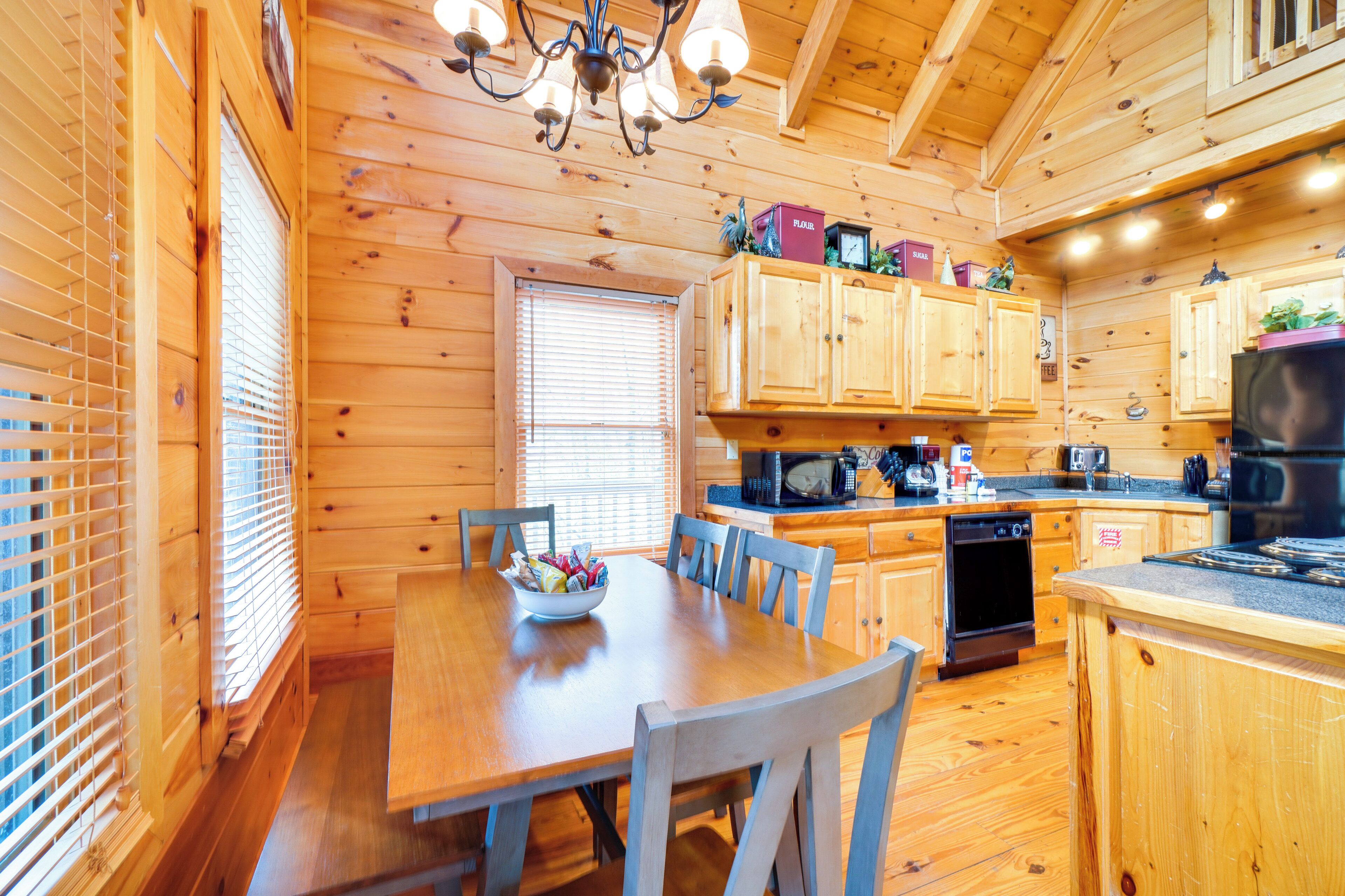 A wooden cabin interior with a dining table, chairs, a kitchen with wooden cabinets, a microwave, and a refrigerator.