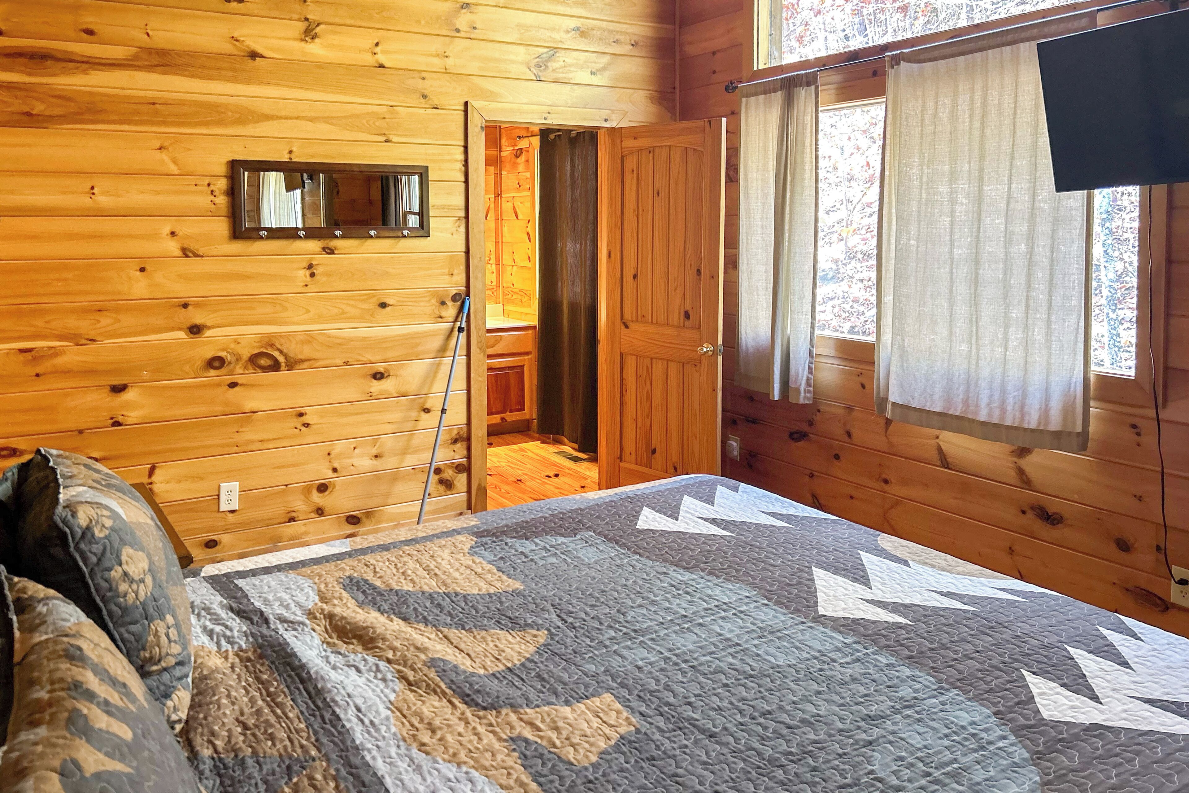 A wooden cabin room with a bed, a quilt, a mirror, and a door leading to a bathroom.