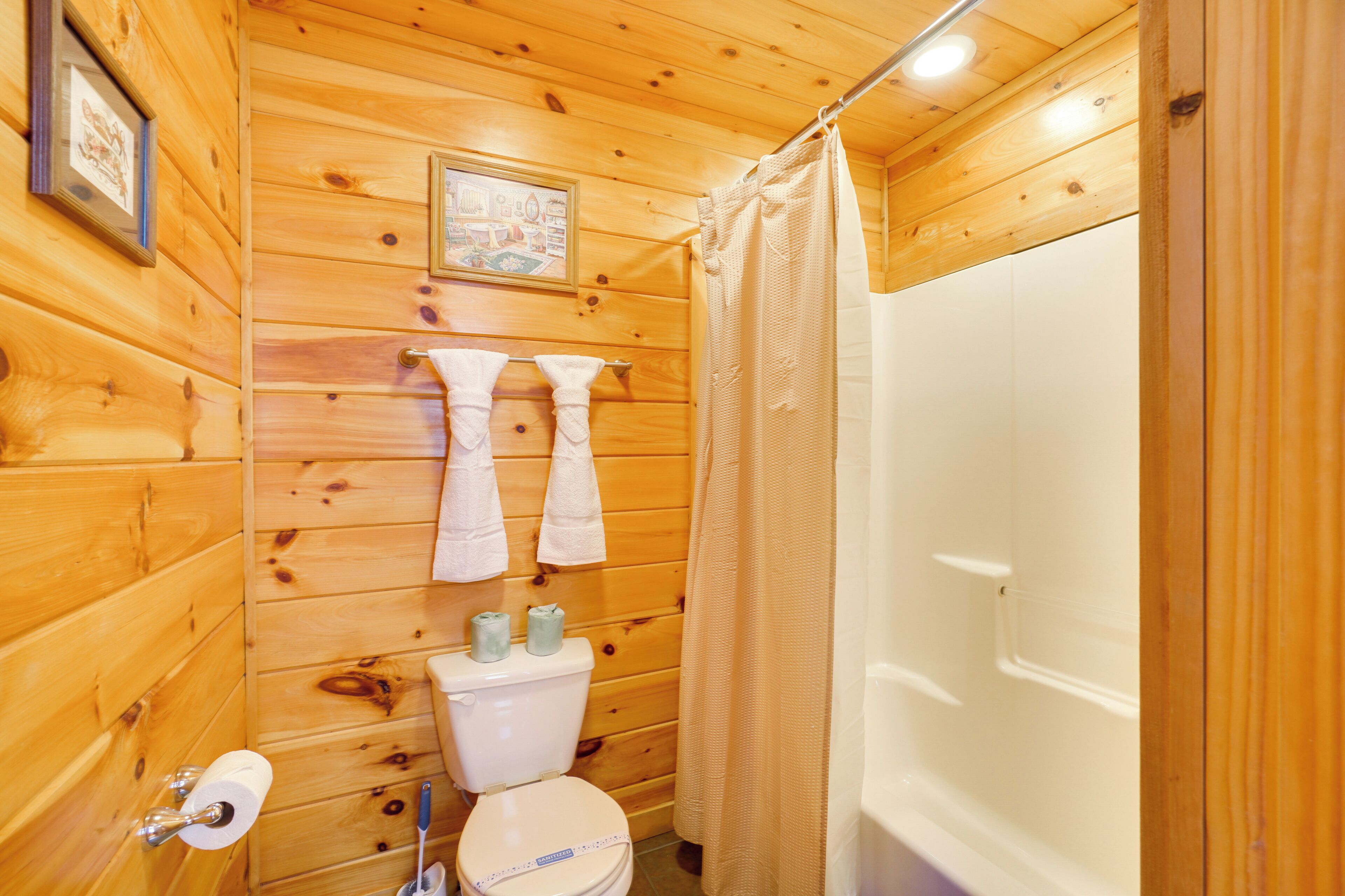 A wooden-paneled bathroom with a toilet, two towels, and a shower curtain.