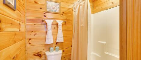 A wooden-paneled bathroom with a toilet, two towels, and a shower curtain.