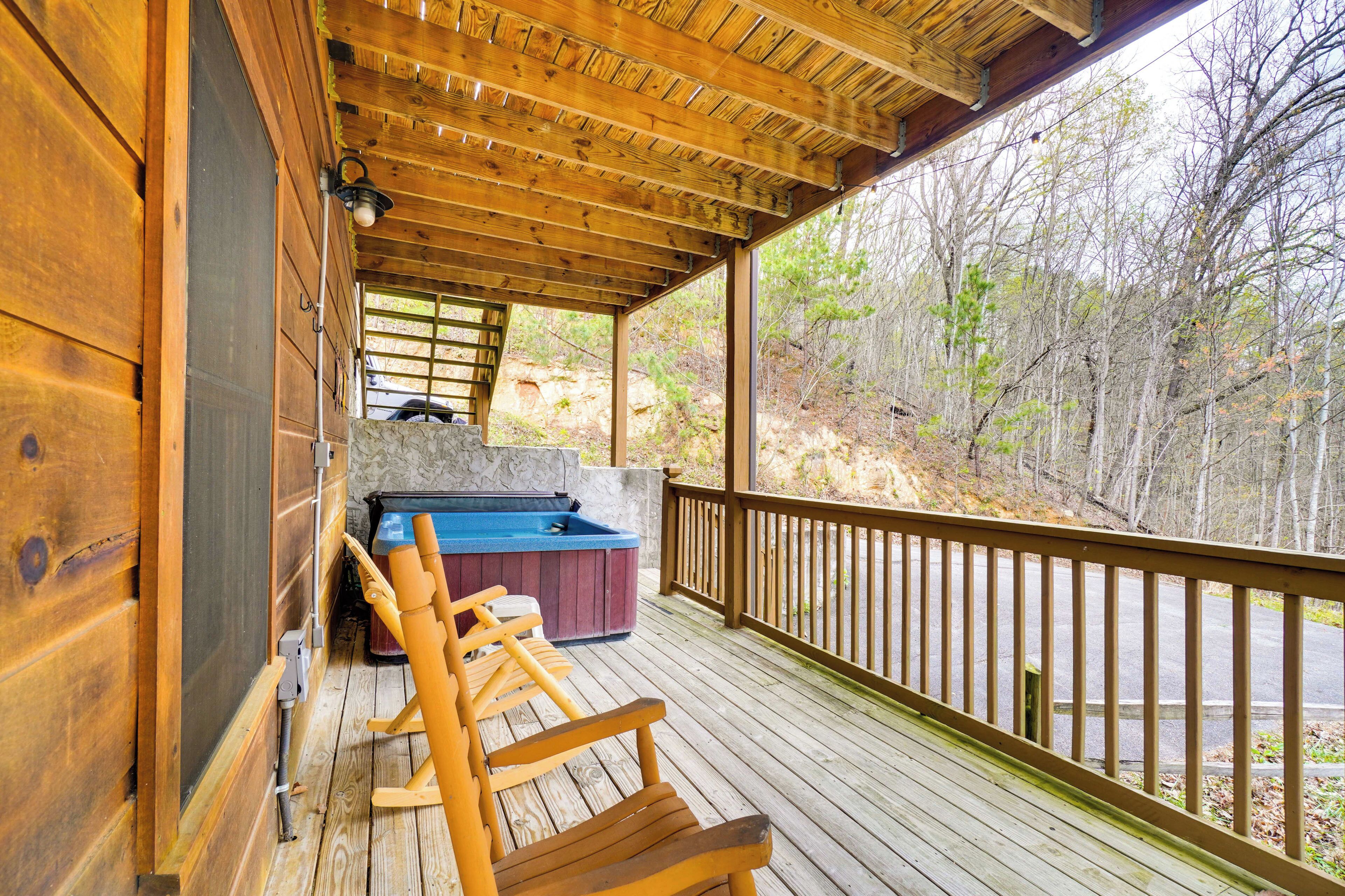 Une terrasse en bois avec un jacuzzi et des fauteuils à bascule, donnant sur une zone boisée.