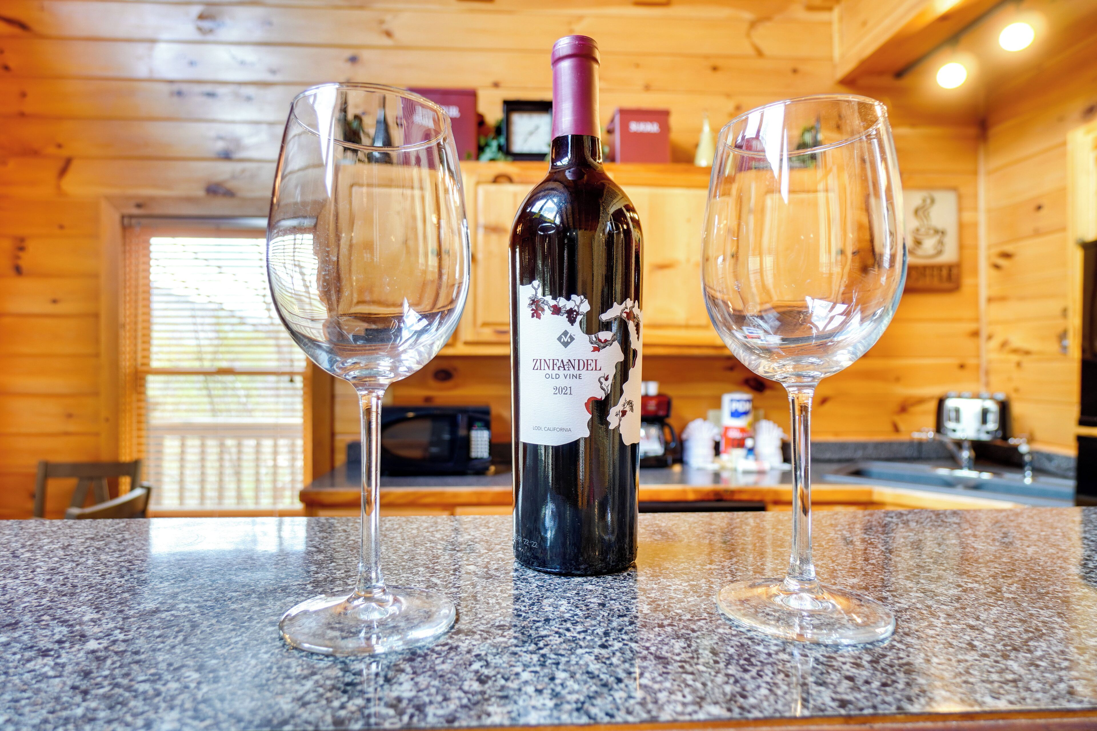 Una botella de vino Zinfandel y dos copas de vino vacías sobre una encimera de granito en el interior de una cabaña de madera.