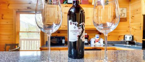 Una botella de vino Zinfandel y dos copas de vino vacías sobre una encimera de granito en el interior de una cabaña de madera.