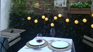 A table set for two with wine glasses and plates, surrounded by greenery and string lights. - Enjoy Valencia. Studio located between Ruzafa and City of Arts and Sciences. (Valencia)