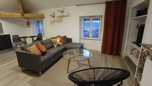 Una sala de estar moderna con un sofá modular gris, una mesa de centro de vidrio, una silla de alambre negra y vistas de la ciudad a través de una ventana.