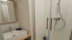 Un baño moderno con ducha envuelta en vidrio, lavamanos blanco y espejo sobre el lavamanos.
