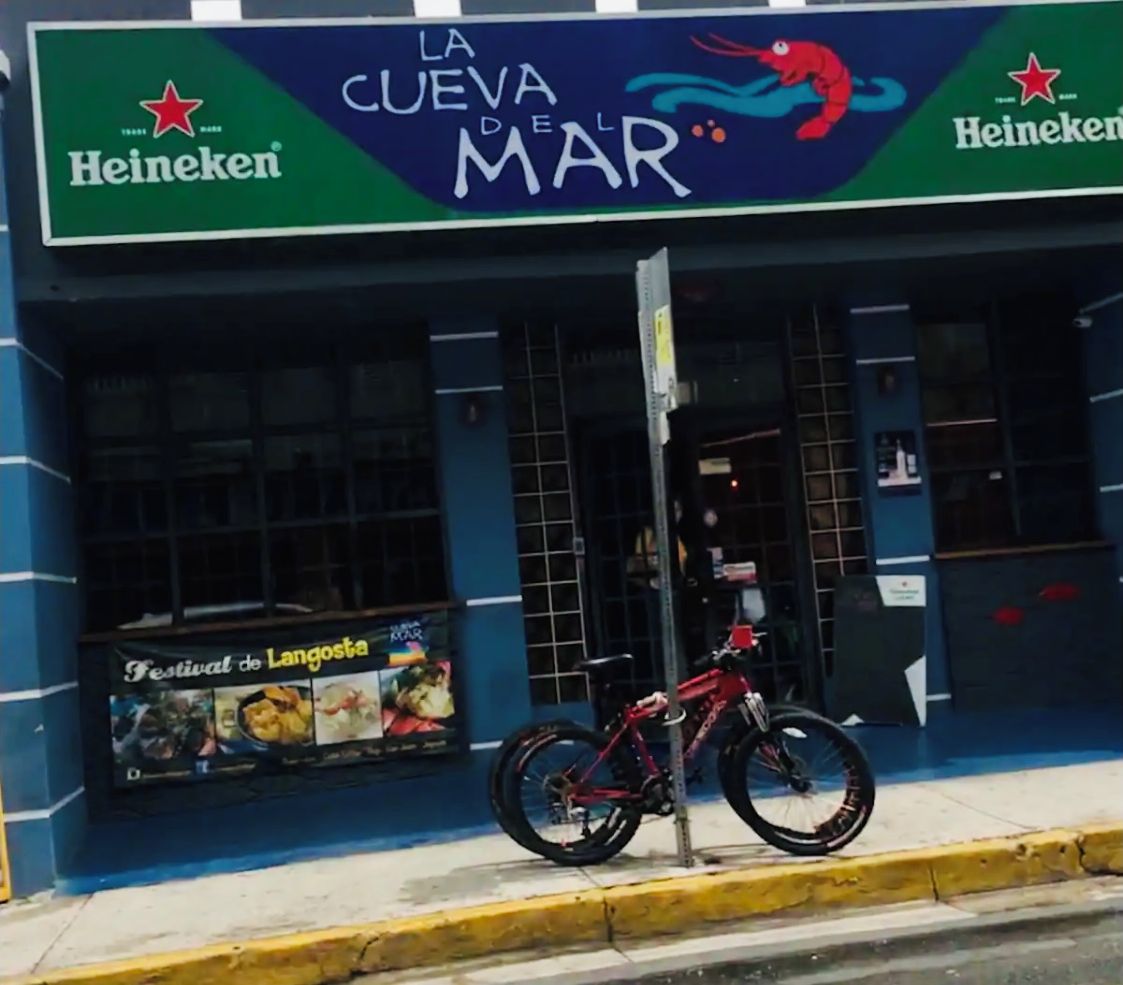 Un escaparate con un letrero que dice "La Cueva del Mar" y la marca "Heineken". Una bicicleta está estacionada al frente.