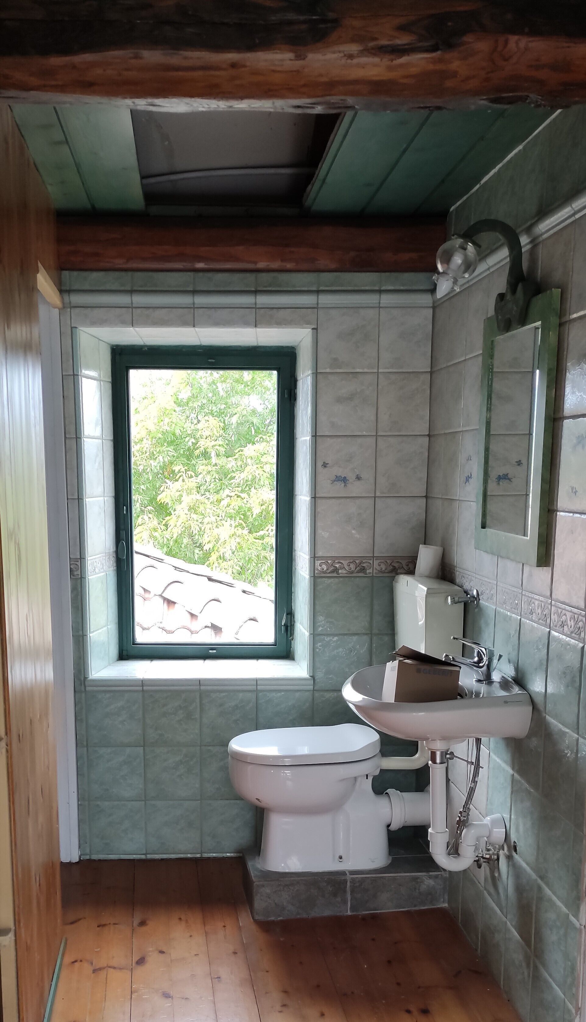 A bathroom with a window, a toilet, a sink, and a mirror.