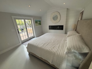 Un dormitorio con una cama grande, un televisor montado en la pared y un ventanal corredero que da a un espacio exterior.