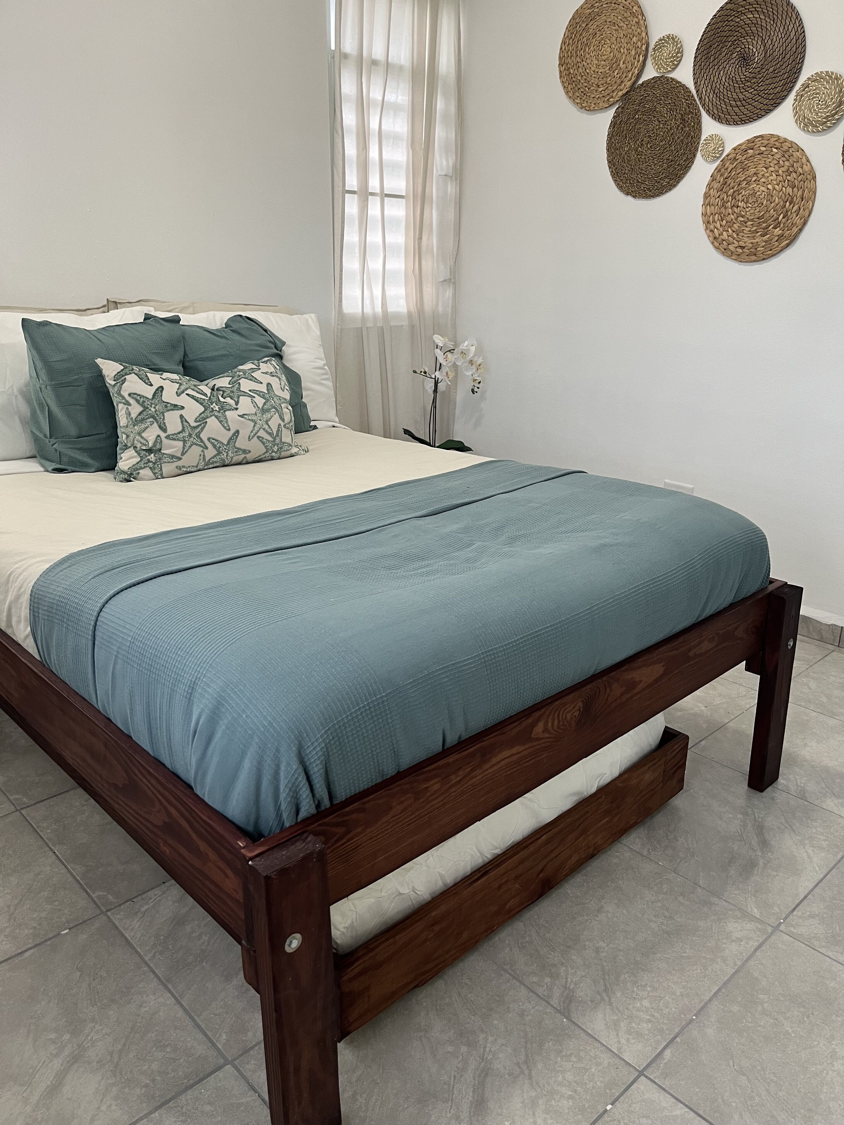 Un letto rifatto con cura, con copriletto e cuscini azzurri, una testiera in legno e una parete decorata con elementi tessili.