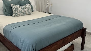 Un letto rifatto con cura, con copriletto e cuscini azzurri, una testiera in legno e una parete decorata con elementi tessili.
