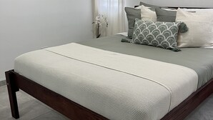 A bedroom with a wooden bed frame, a grey mattress, and a white throw blanket.
