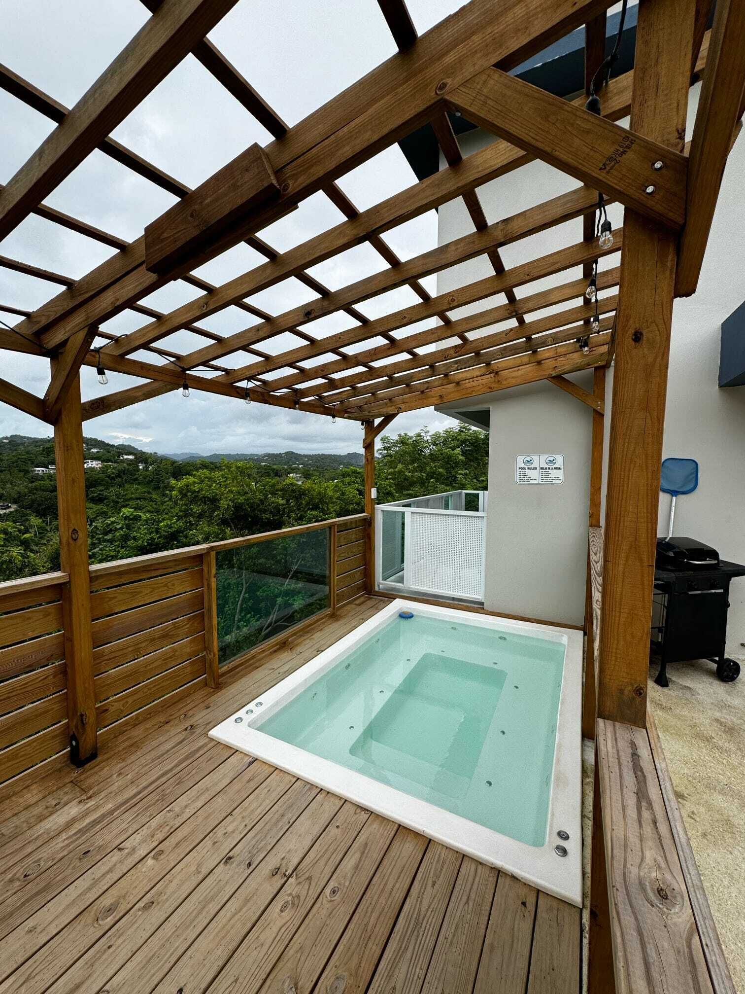 Une terrasse en bois avec un jacuzzi, une pergola et une vue sur le paysage environnant.