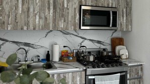 A modern kitchen with a marble backsplash, a built-in microwave, a gas stove, and a hanging pendant light.