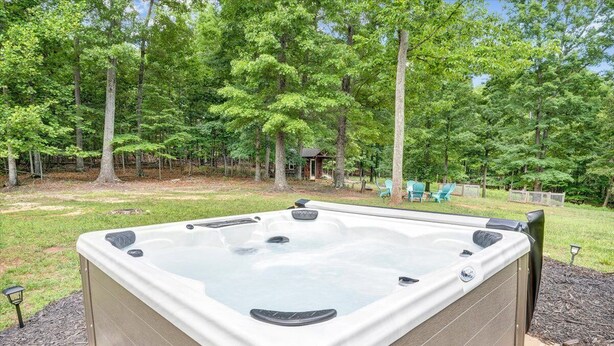 Un jacuzzi en un patio trasero con terraza de madera, rodeado de árboles y un cobertizo pequeño.