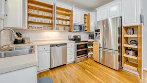 Una cocina moderna con armarios blancos, electrodomésticos de acero inoxidable y estantes de madera.
