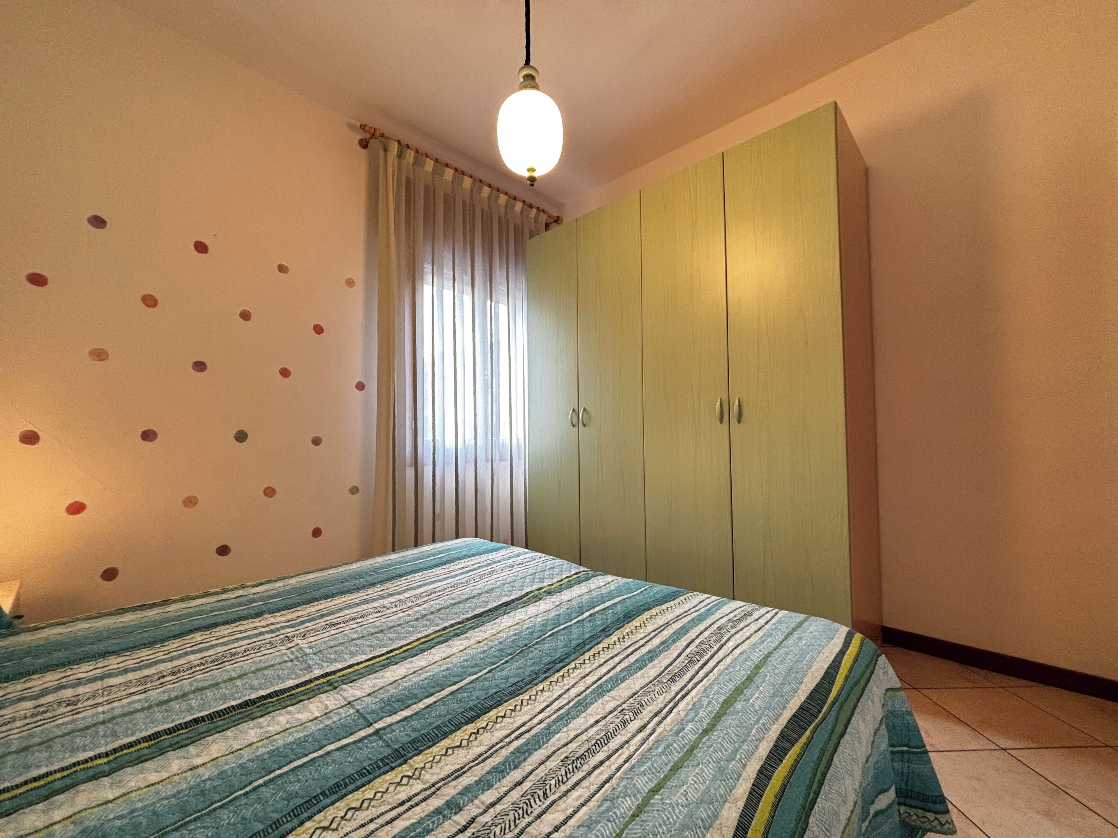 A bedroom with a bed, a wardrobe, a curtain, and a wall with circular patterns.