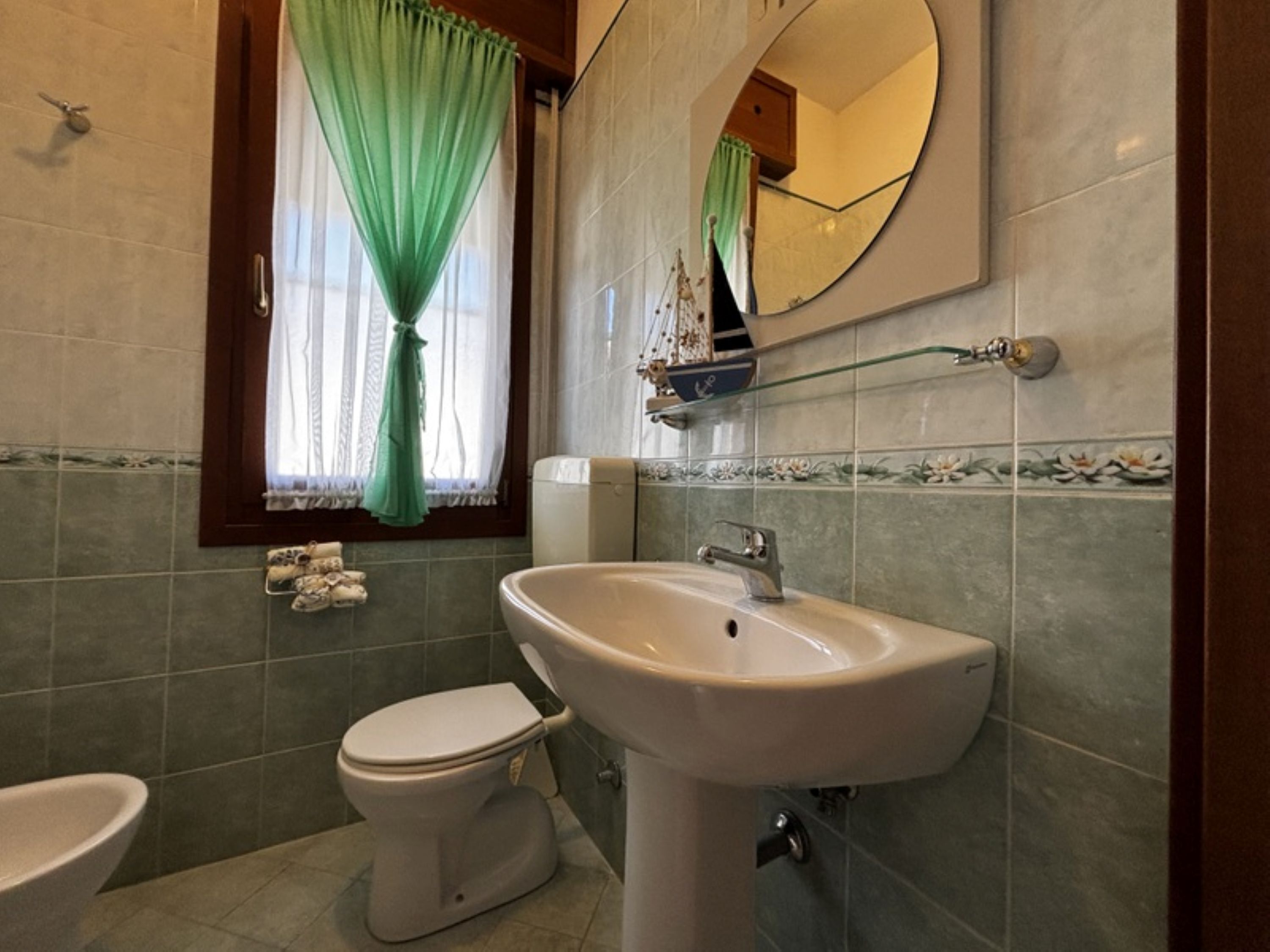 A bathroom with a toilet, sink, and window with green curtains.
