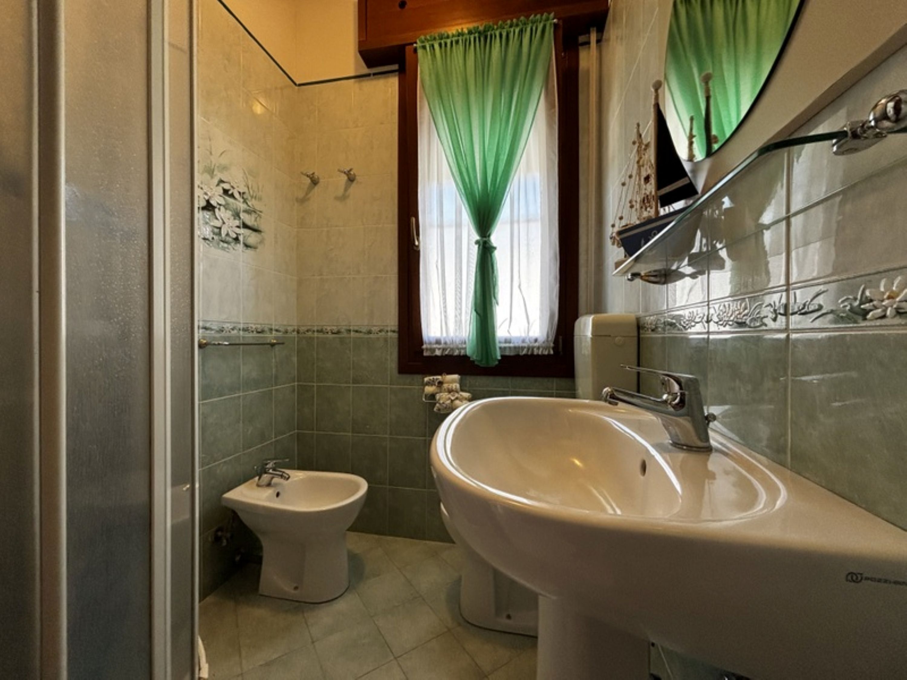 Een badkamer met een bidet, een wastafel en een raam met groene gordijnen.
