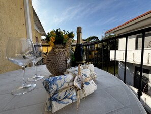 A round table with two wine glasses, a bottle of champagne, a woven basket with flowers, and a cloth with a blue pattern. - Renovated Apartment in Rosolina (Rosolina)