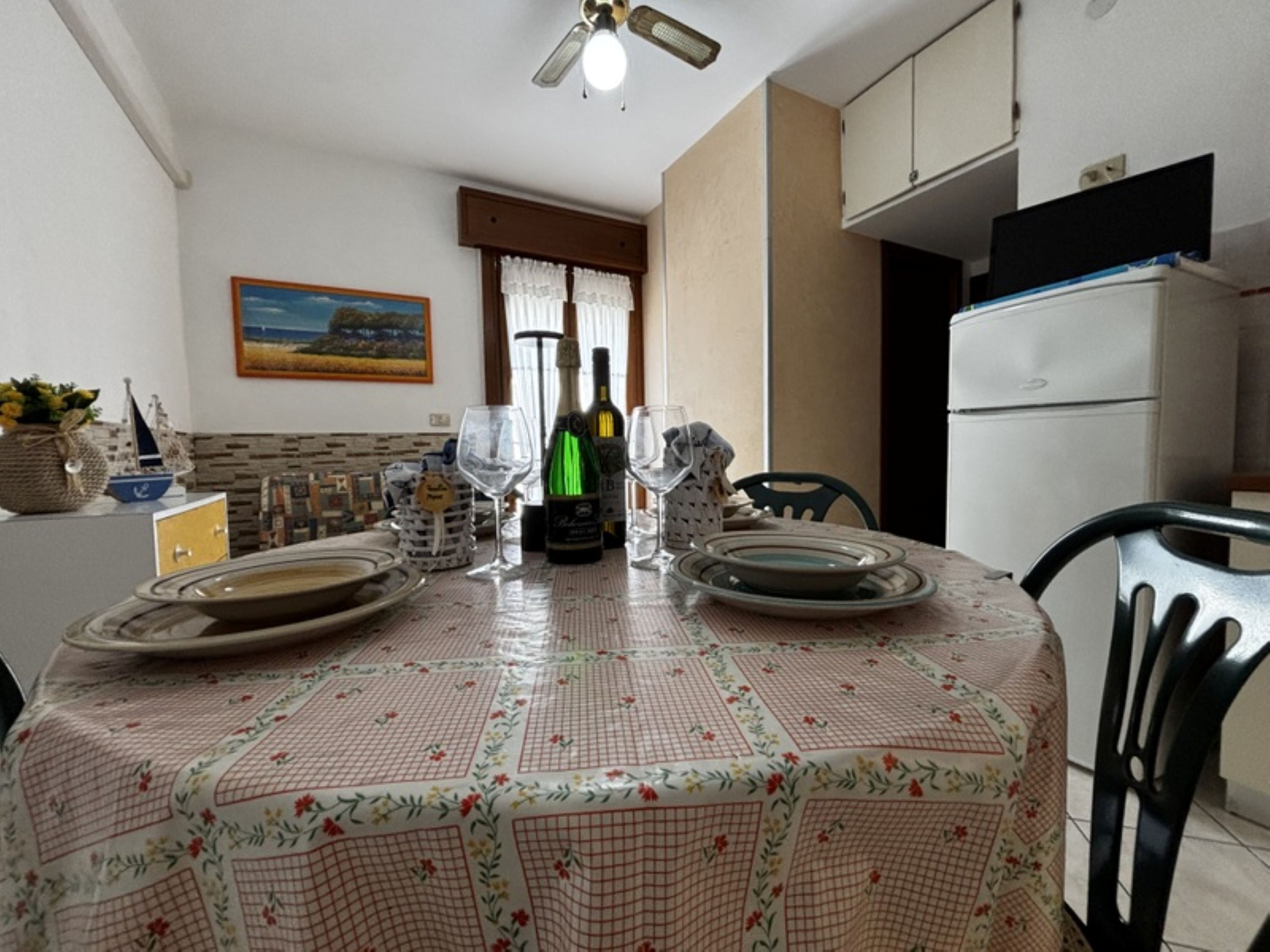 A dining table with a floral tablecloth, two wine glasses, and a bottle of wine.