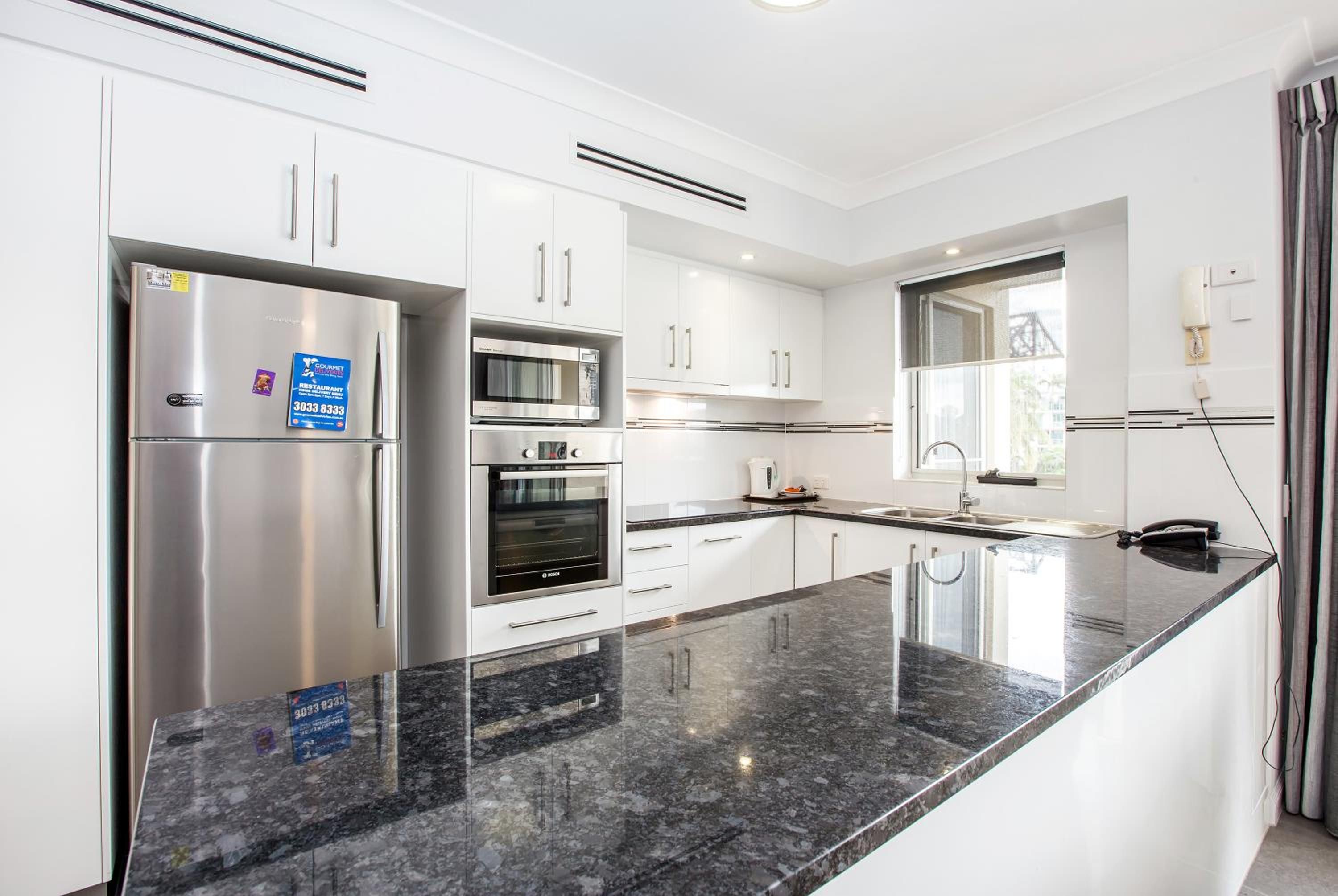 A modern kitchen with stainless steel appliances, white cabinetry, and a granite countertop.