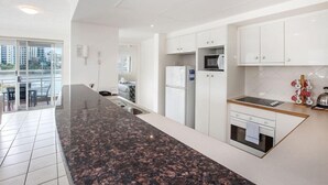 A modern kitchen with white cabinets, a granite countertop, a built-in oven, and a microwave. - Bridgewater Terrace (Brisbane)
